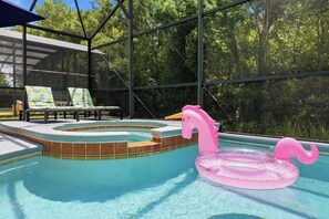 A swimming pool with a hot tub, surrounded by a glass enclosure, and a pink flamingo float. - Private Pool & Game Room Near Disney Parks (Kissimmee)