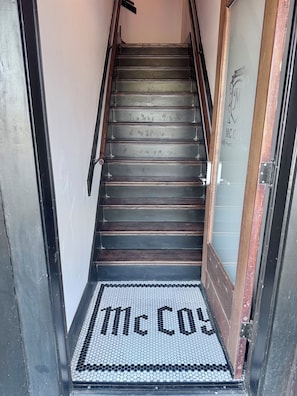 A staircase with wooden steps and a metal railing, leading to a door with a frosted glass panel and a sign that reads 'McCoy Place'. - Lily's Oasis located in recently renovated historic McCoy Place Lofts. (Cave City)
