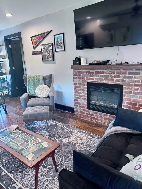 Una sala de estar con chimenea, televisor montado en la pared y una mesa de centro con revistas.