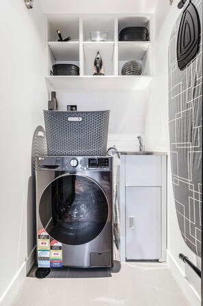 A compact laundry room with a front-loading washing machine, a dryer, and storage shelves above. - VAQUAY The Sable Gallery In Melbourne CBD (Melbourne)