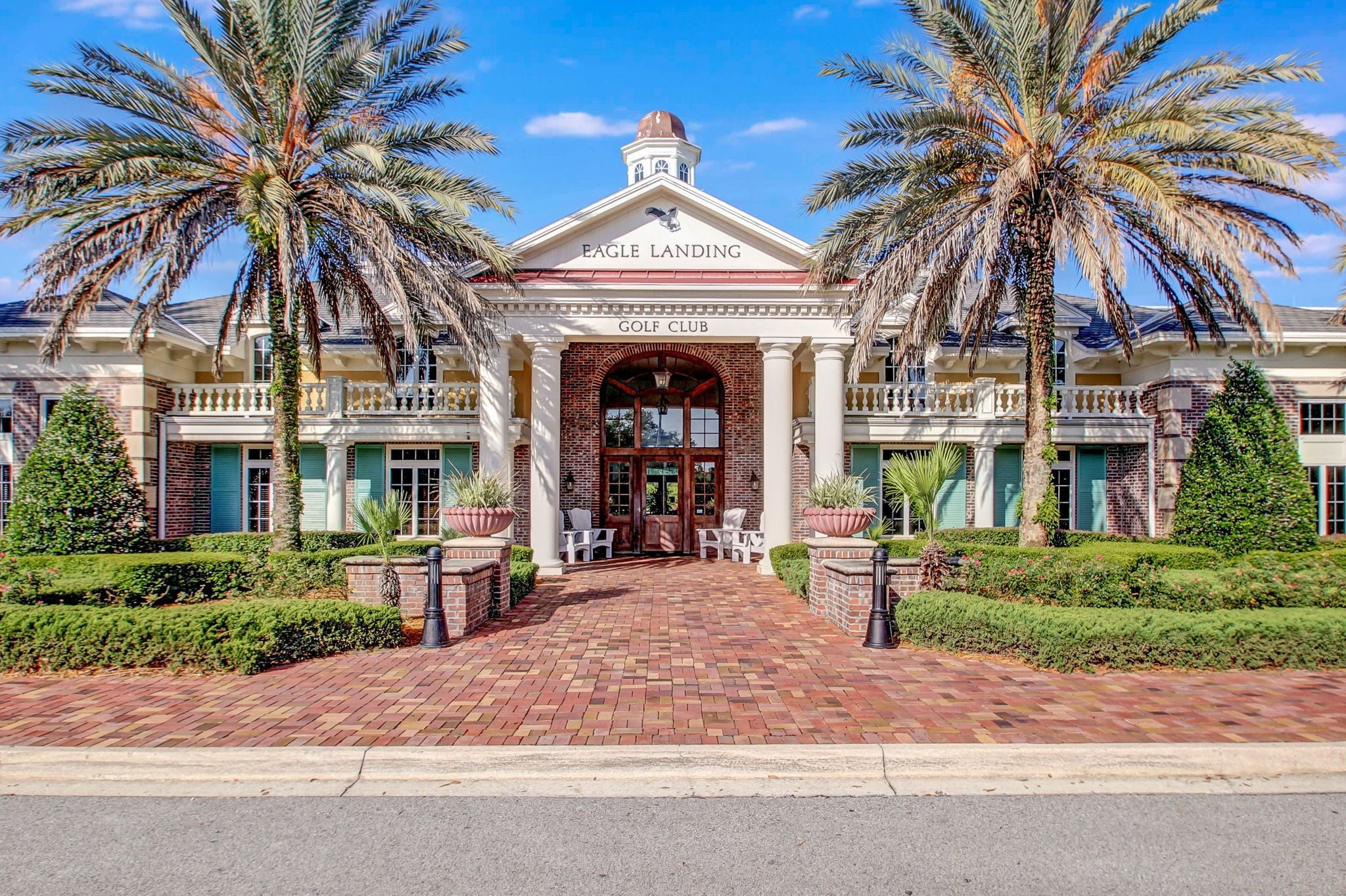 Un edificio con entrada central, flanqueado por palmeras, con el rótulo 'Eagle Landing Golf Club'.