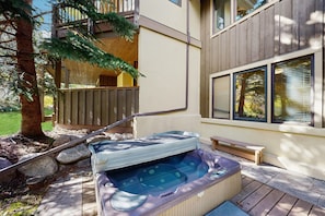 Un jacuzzi en una terraza de madera con un cerco de madera y un árbol al fondo.
