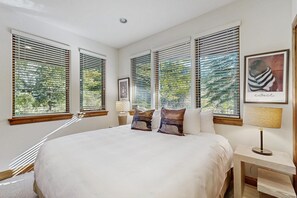 A bedroom with a large bed, multiple windows with blinds, a bedside table with a lamp, and a framed picture on the wall. - East Vail home with private hot tub, A/C and Vail Village ski lockers (Vail)
