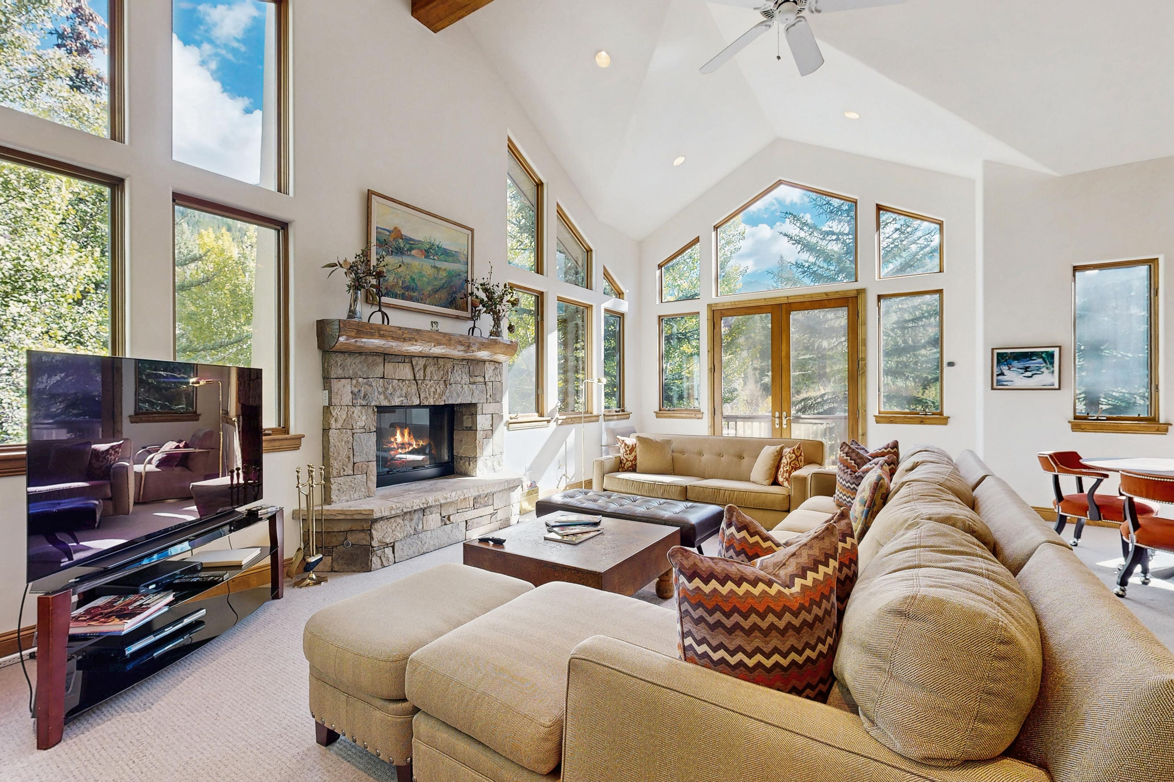 A spacious living room with a stone fireplace, large windows, and a television.