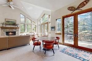 A spacious living room with a fireplace, a dining area with a round table, and large windows offering views of the outdoors. - East Vail home with private hot tub, A/C and Vail Village ski lockers (Vail)