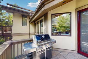 A patio with a Weber Genesis grill, a wooden deck, and a view of a backyard with a table and chairs. - Spacious East Vail retreat with 4 bedrooms, private hot tub, and amazing location (Vail)