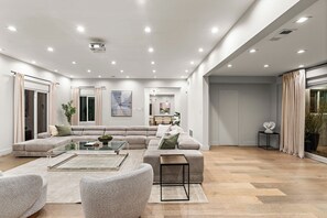 A spacious living room with a large sectional sofa, a glass coffee table, and a modern fireplace. - Varna Garden House By Alora Reserve (Los Angeles)