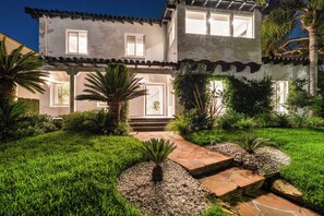 Una casa de dos pisos con un jardín cuidado, un camino de piedra y una palmera.