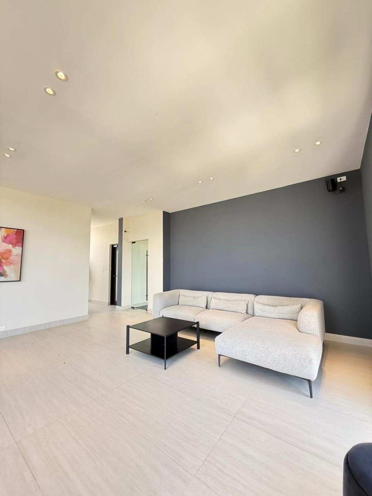 Ein modernes Wohnzimmer mit einem Ecksofa, einem Couchtisch und Einbau-Deckenleuchten.