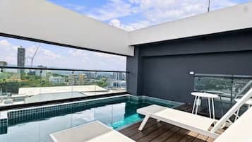 Ein Infinity-Pool auf dem Dach mit weißen Liegestühlen und einer Glasbrüstung.
