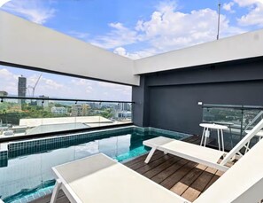 Una piscina infinita en la azotea con sillones blancos y barandilla de cristal.