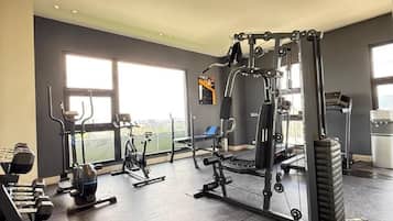 Ein Fitnessstudio mit verschiedenen Trainingsgeräten, großen Fenstern und Blick ins Freie.
