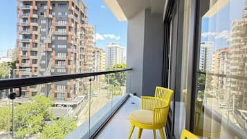 Ein Balkon mit gelben Stühlen, einer Glasumlaufung und Blick auf die umliegenden Gebäude.