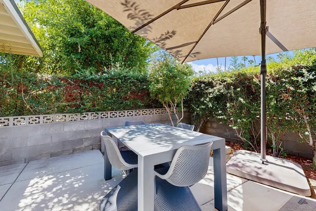 An outdoor patio with a table and chairs, surrounded by greenery and a patterned wall.