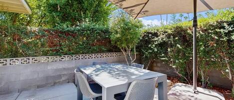 An outdoor patio with a table and chairs, surrounded by greenery and a patterned wall.