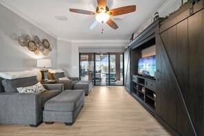 A modern living room with a ceiling fan, a flat-screen TV, and a seating area with sofas and ottomans. - Waterfront Paradise, Private Dock, 4BR, 2 bath,  Private Pool & Mins to Downtown (Punta Gorda)