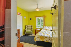 Una habitación con cama, una silla, un escritorio, una ventana y un letrero de salida.
