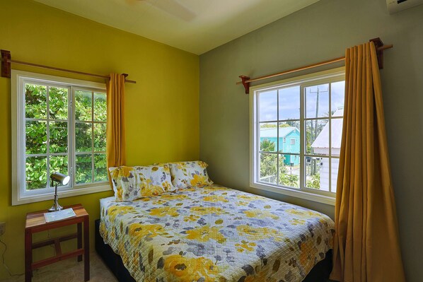 Un dormitorio con cama, dos ventanas, una mesita de noche y una lámpara.
