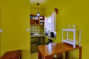 Una cocina compacta con una mesa de madera, una lámpara colgante y un ventanal con cortinas.