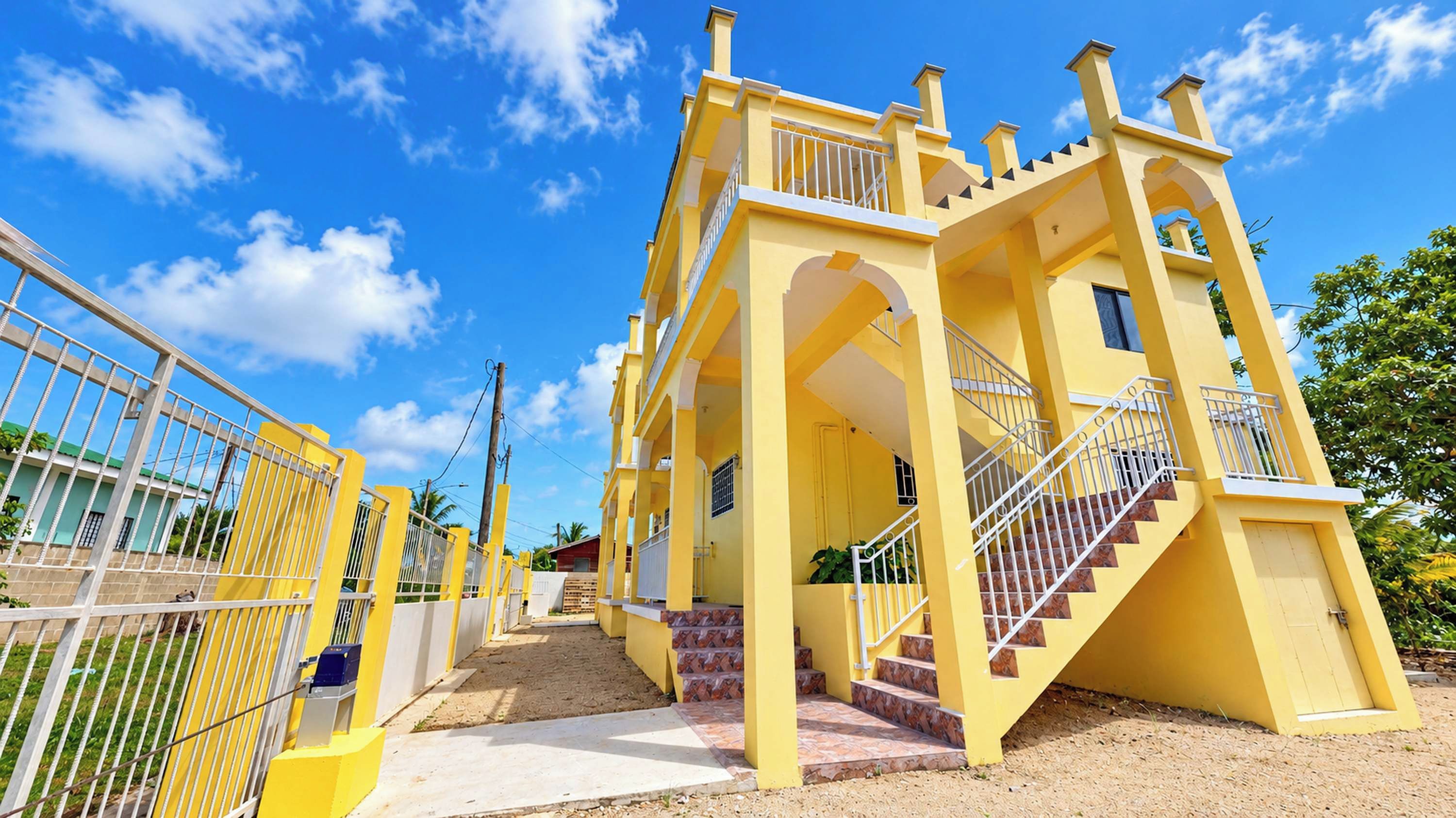 A yellow building with a staircase leading to an upper level, surrounded by a fence.