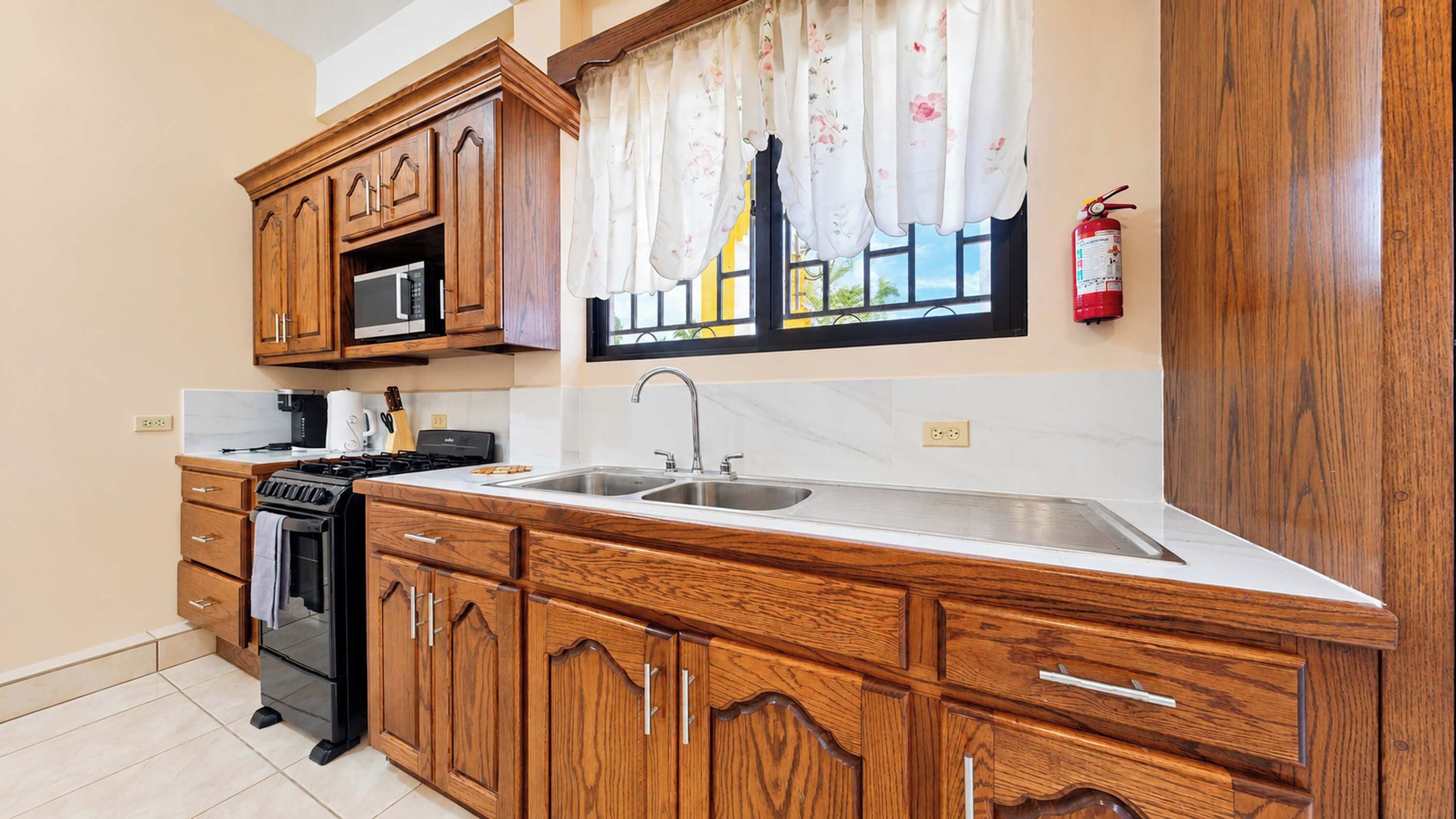 Una cocina con armarios de madera, un lavamanos de acero inoxidable, un microondas y una estufa.