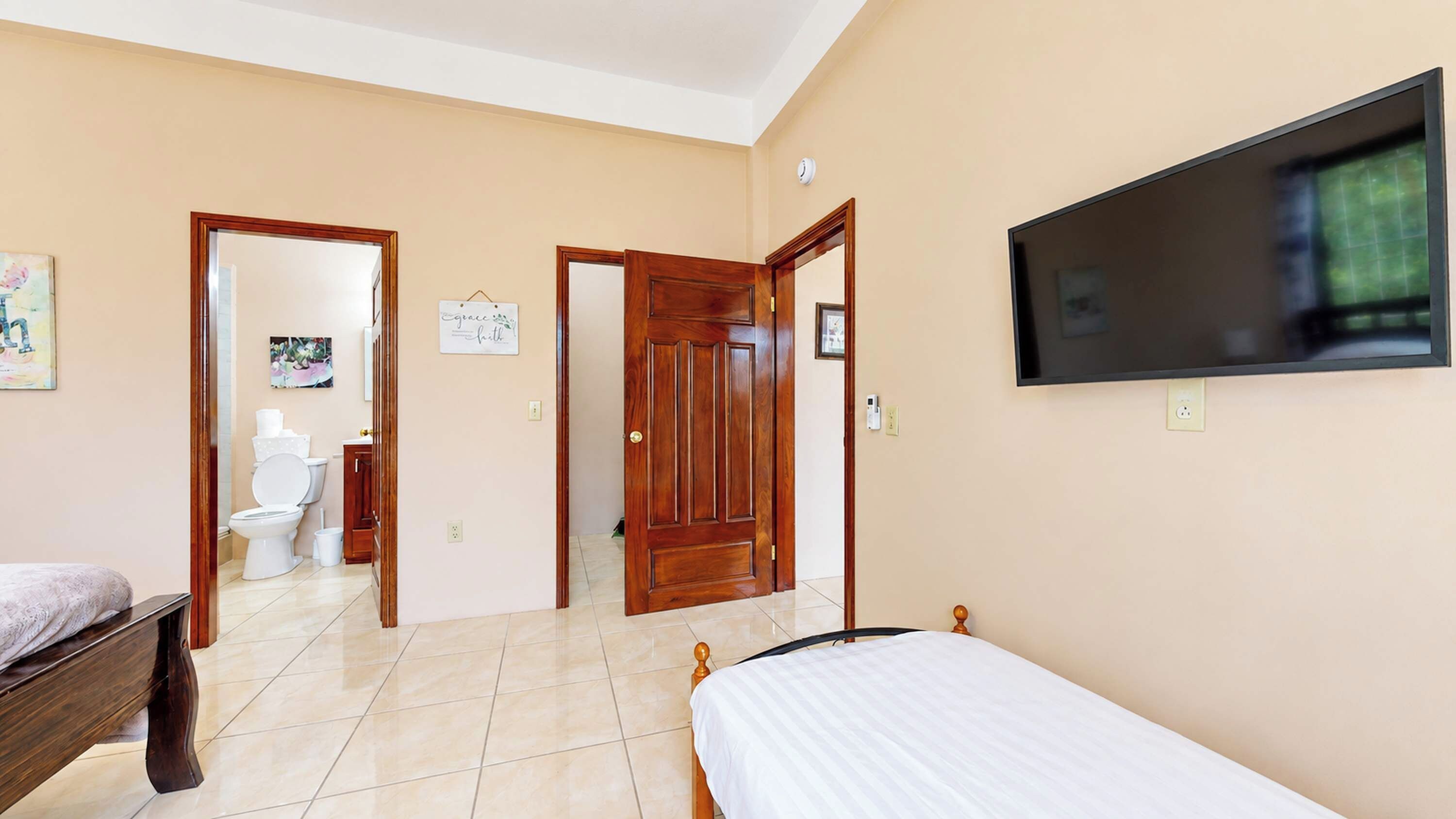 A bedroom with a bed, a TV, a wooden door, and a bathroom visible through an open door.