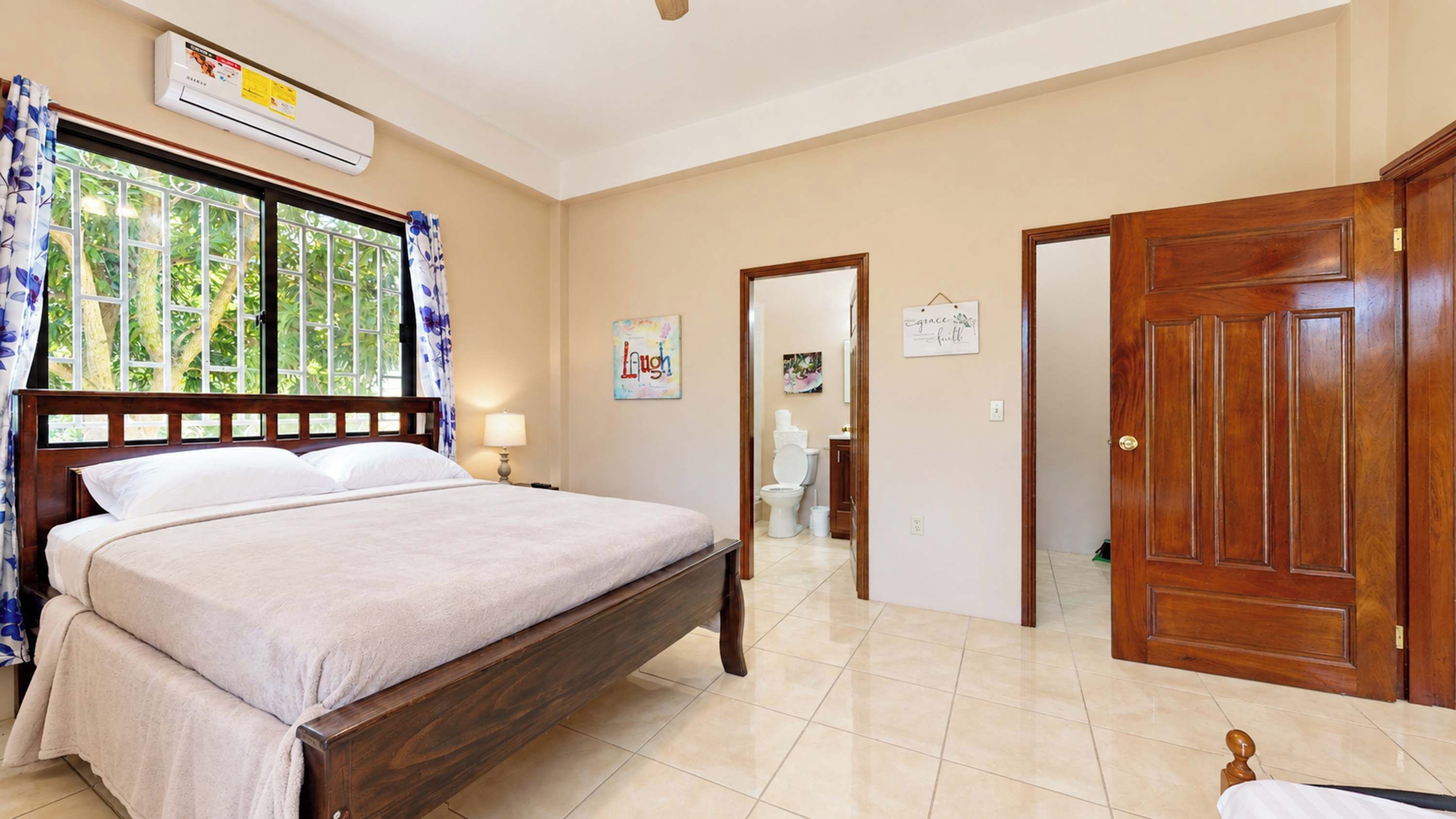 Un dormitorio con una cama, una ventana con cortinas, una puerta y un equipo de aire acondicionado instalado en la pared.