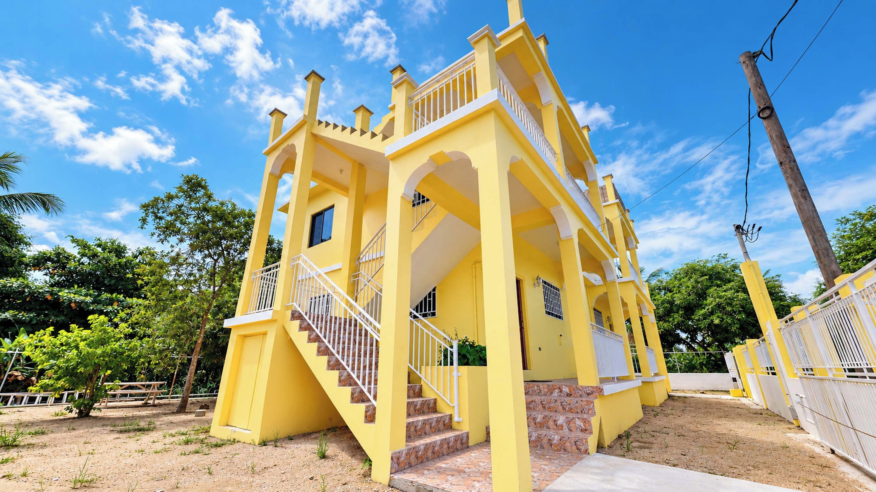 A yellow building with a staircase, multiple balconies, and a fenced area.