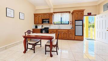 A kitchen with wooden cabinets, a dining table, chairs, a refrigerator, and a window with curtains.
