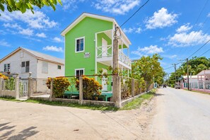 Un immeuble de deux étages avec une façade verte, un balcon et une pancarte indiquant qu’il est à vendre.