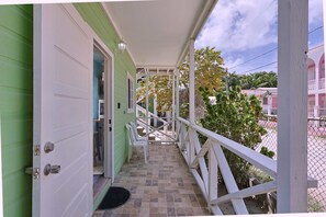 A covered porch with a tiled floor, a white railing, and a door leading to a room. - Central Caye Caulker Apartment w/ AC, Wi-Fi & Kitchen | Unit 2 (Caye Caulker)