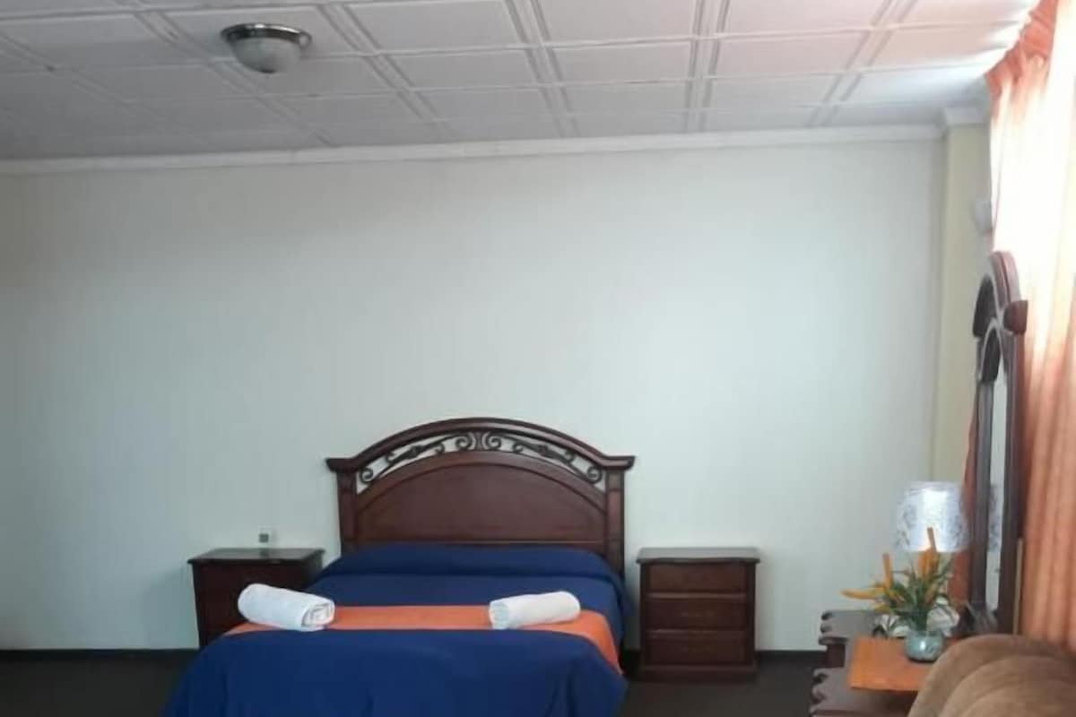 A hotel room with a bed, a chair, a nightstand, and a lamp.