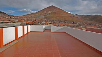 A rooftop terrace with a view of a mountain and a town below.
