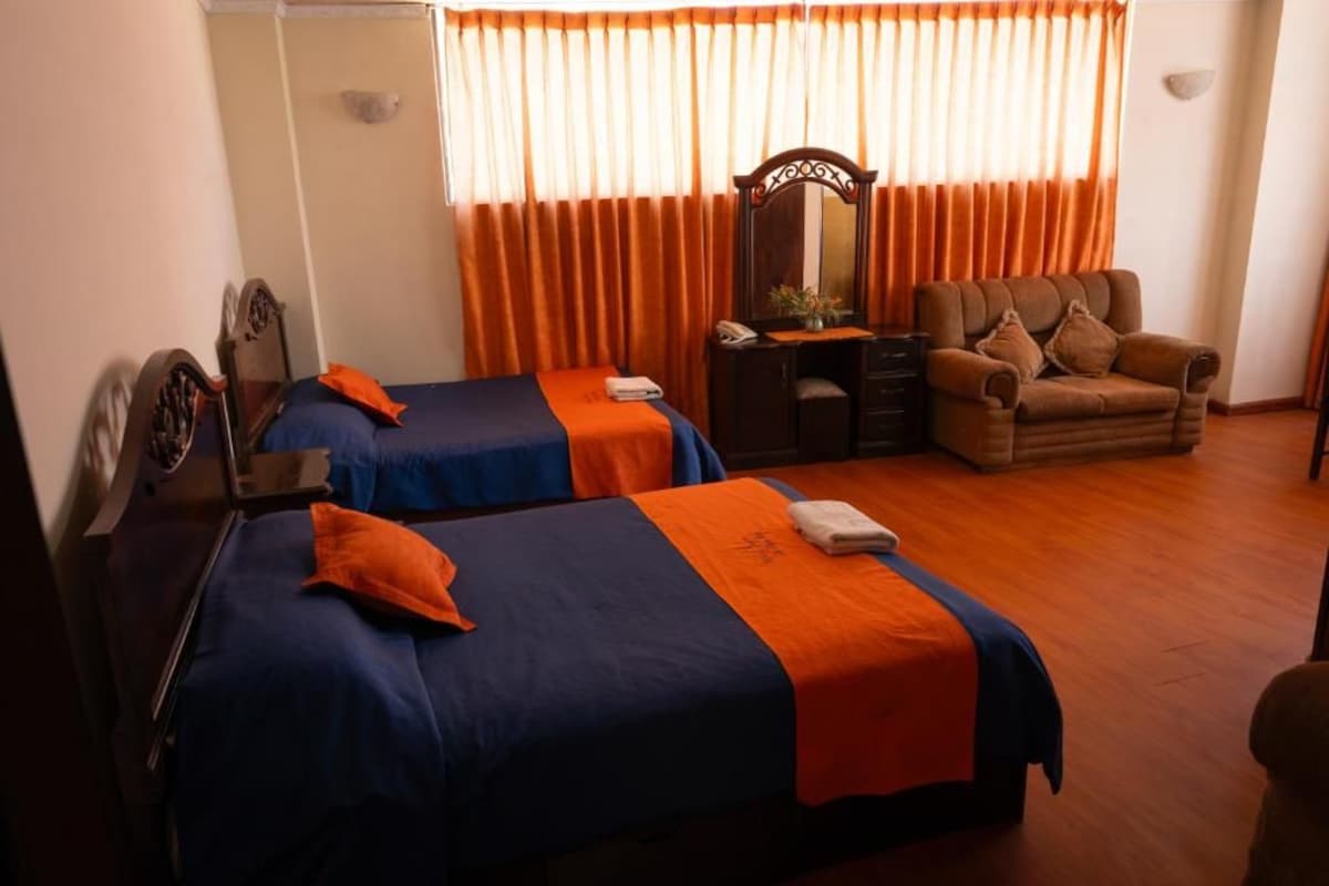 A hotel room with two beds, a desk, a chair, a mirror, and a window with curtains.