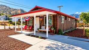 A wooden cabin with a porch, red chairs, and a hanging American flag. - 5 Mins from Lake/AC/Kids+Pets/Fenced Yard/Toys (Lake Isabella)