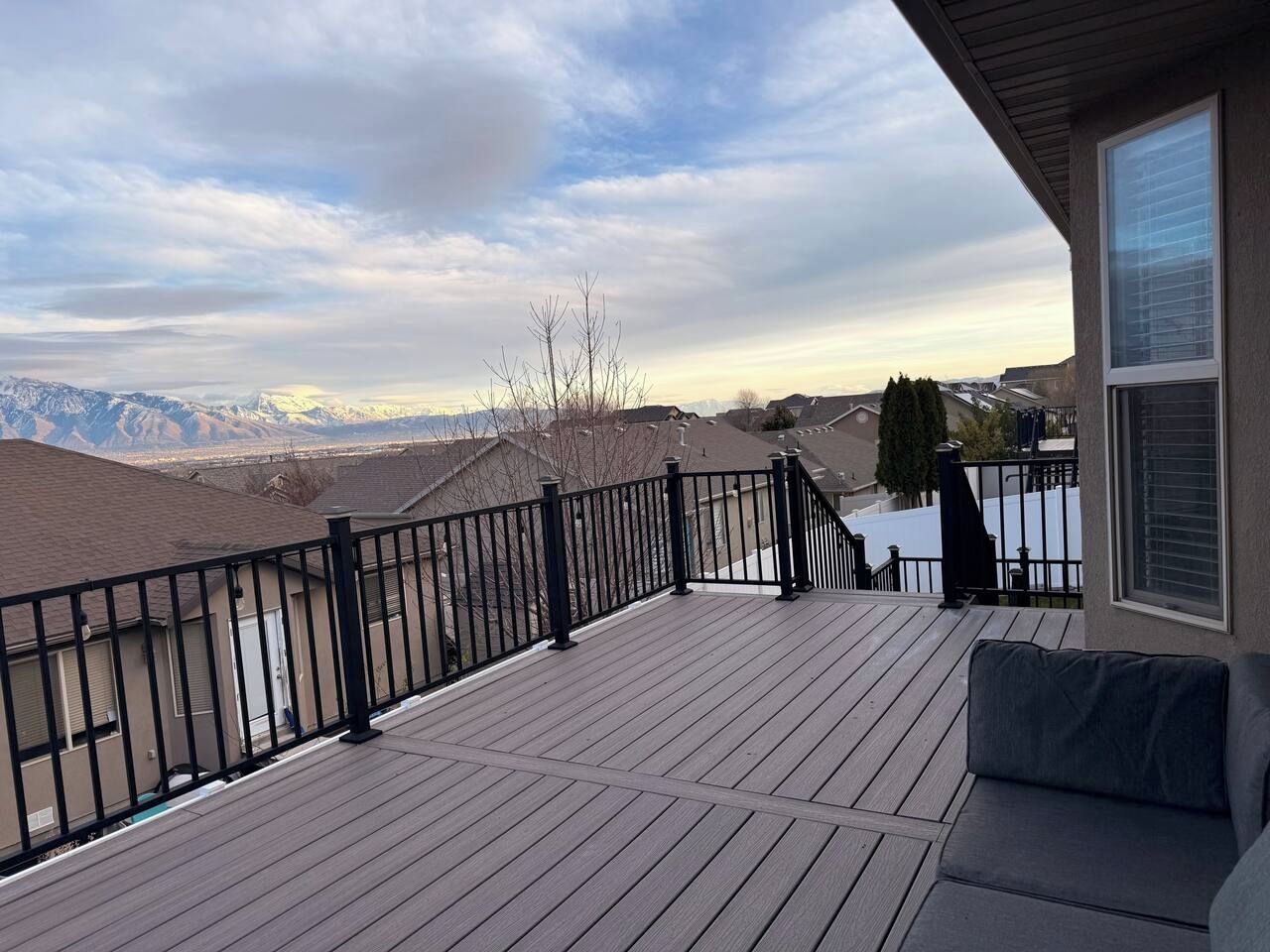 A deck with a black railing, a sofa, and a view of a snowy mountain range.