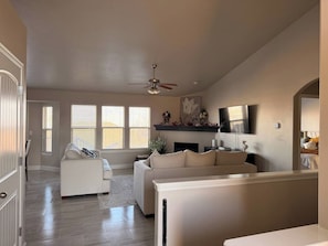 A spacious living room with a fireplace, a ceiling fan, and a television. - Modern Retreat, Cozy, Calm & Perfectly Located (West Jordan)