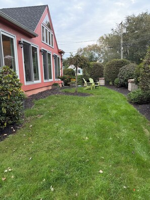 Una propiedad residencial con un césped bien cuidado, una casa roja con detalles blancos y un pequeño jardín con un banco y plantas en macetas.