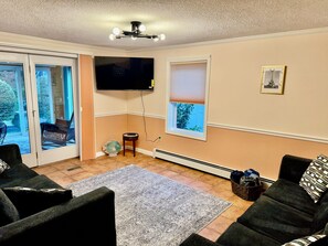 Una sala de estar con una televisión de pantalla plana, un calentador con forma de pez y vistas al exterior a través de una puerta corrediza de vidrio.