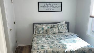 Un dormitorio con una cama, ventilador de techo, una cita enmarcada en la pared y una ventana.