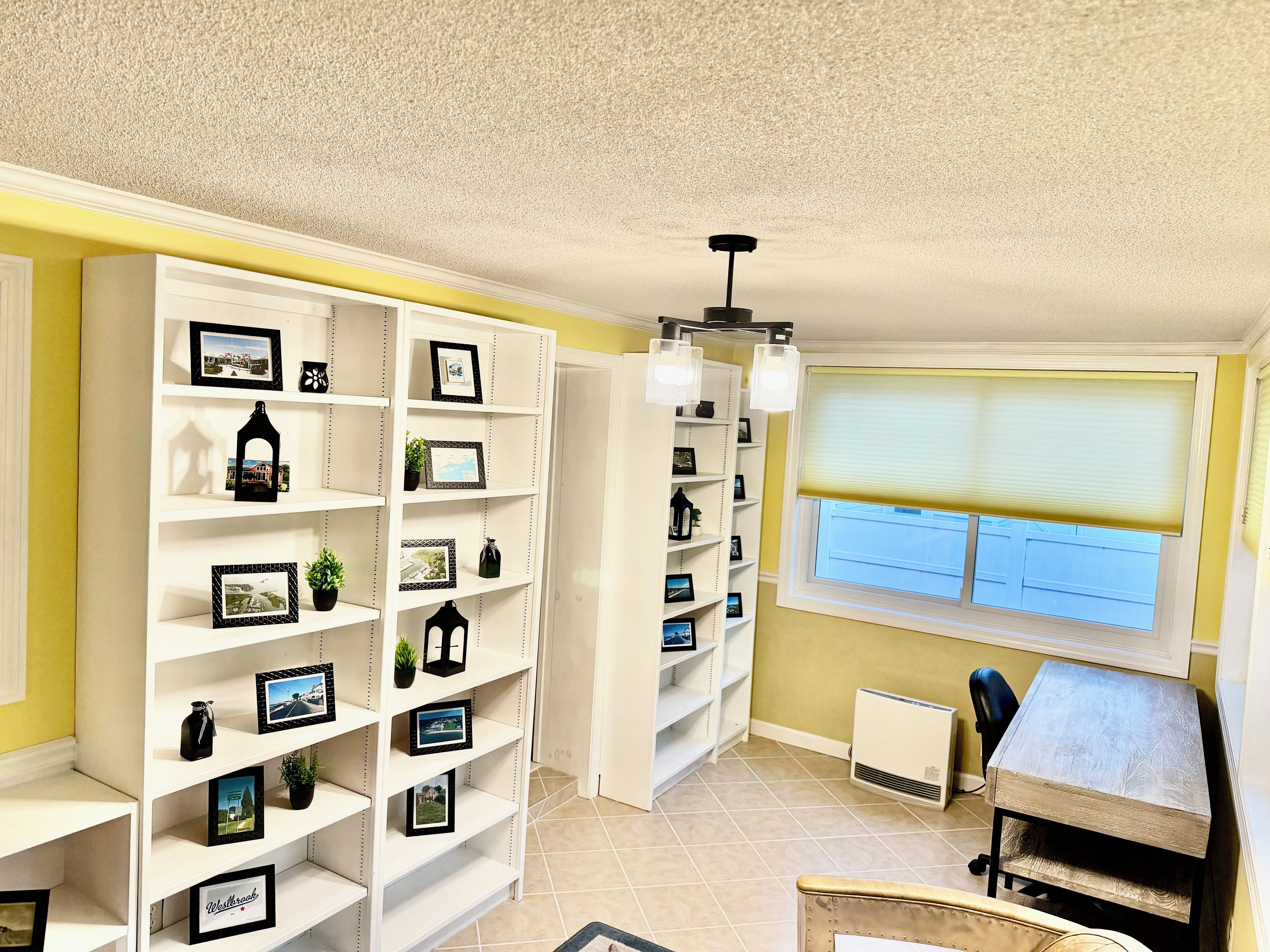 A room with white shelving units filled with framed photos and decorative items, a window with blinds, and a radiator.