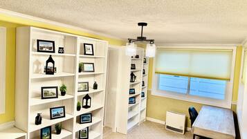 A room with white shelving units filled with framed photos and decorative items, a window with blinds, and a radiator.