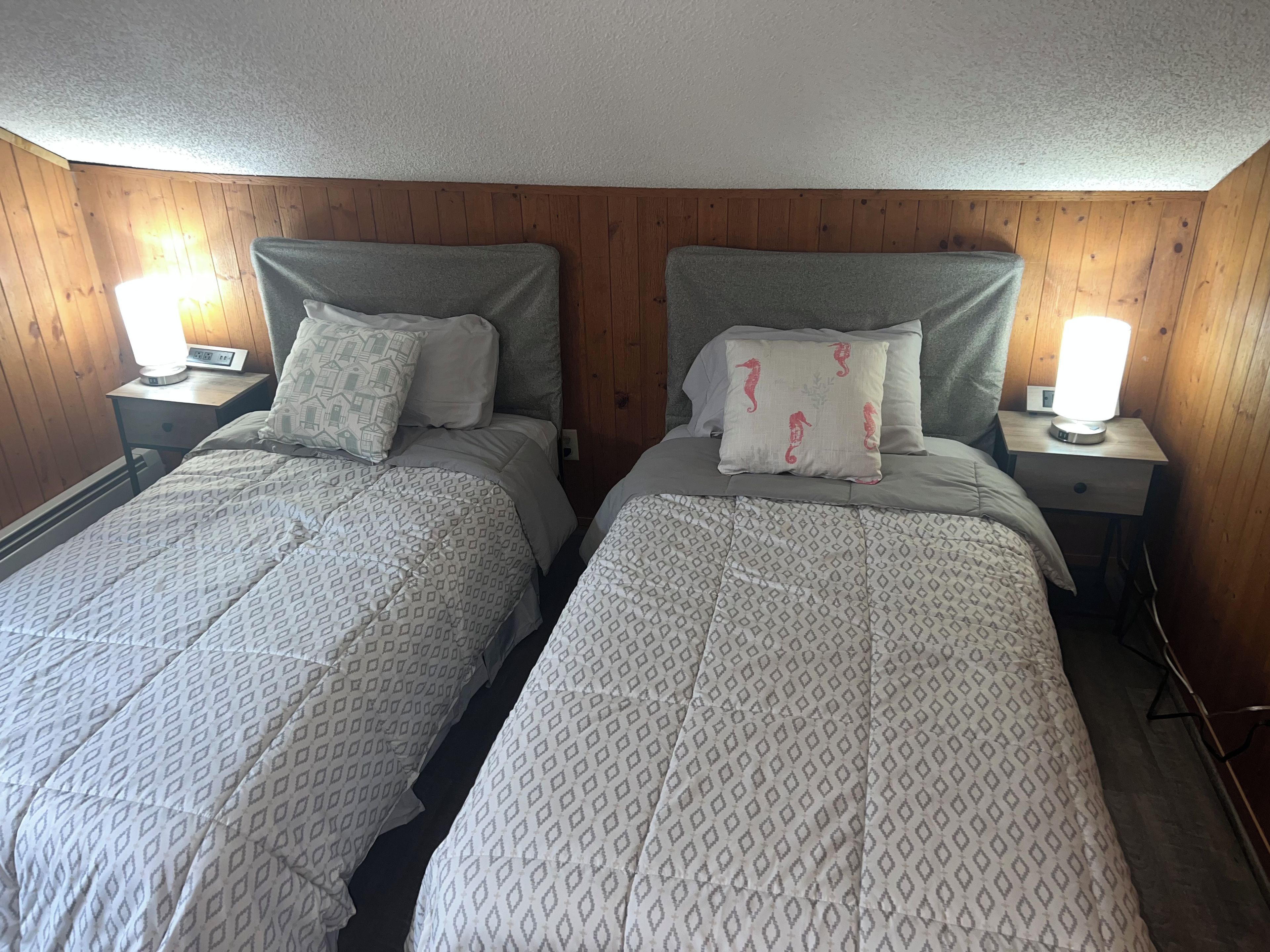 Deux lits jumeaux avec une literie à motifs, des têtes de lit en bois, des lampes de chevet et un mur en bois.