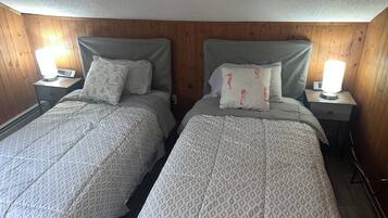 Dos camas individuales con ropa de cama estampada, cabeceros de madera, lámparas de noche y una pared de madera.