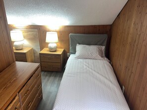 Una habitación pequeña y acogedora con una cama individual, una mesita de noche de madera con lámpara y un aparador con cajones.