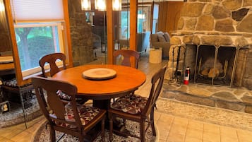 A dining area with a round wooden table, four chairs, and a stone fireplace.