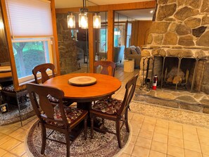 Un comedor con una mesa de madera redonda, cuatro sillas y una chimenea de piedra.
