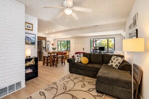 A living room with a sofa, a dining table, and chairs. There is a ceiling fan and a lamp. - Westside Bungalow | King Bed + Fenced Yard + Pets! (Colorado Springs)