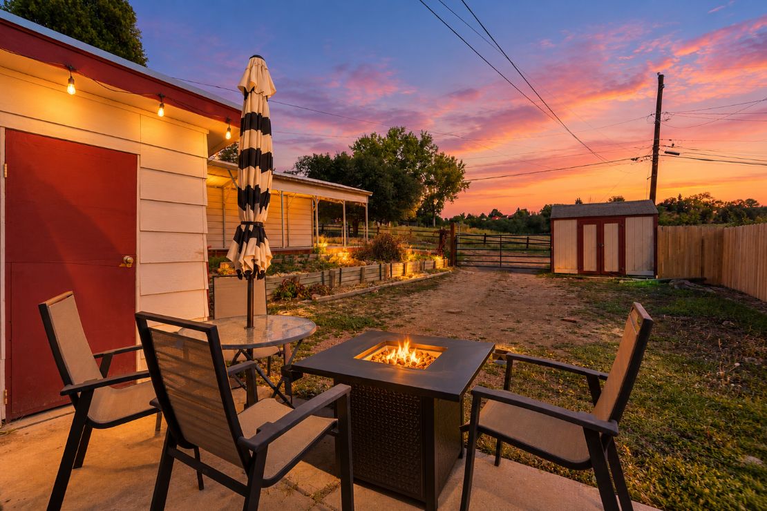 An outdoor patio with a square fire pit, chairs, and an umbrella.