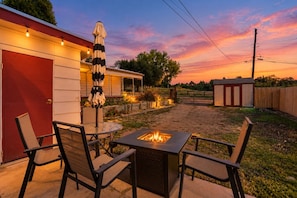 An outdoor patio with a square fire pit, chairs, and an umbrella. - Westside Bungalow | King Bed + Fenced Yard + Pets! (Colorado Springs)